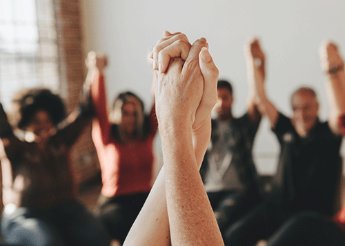 Clasped hands of two people in an intensive outpatient program with others