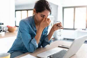 woman sitting at desk experiencing physical symptoms of depression like blurry eyes